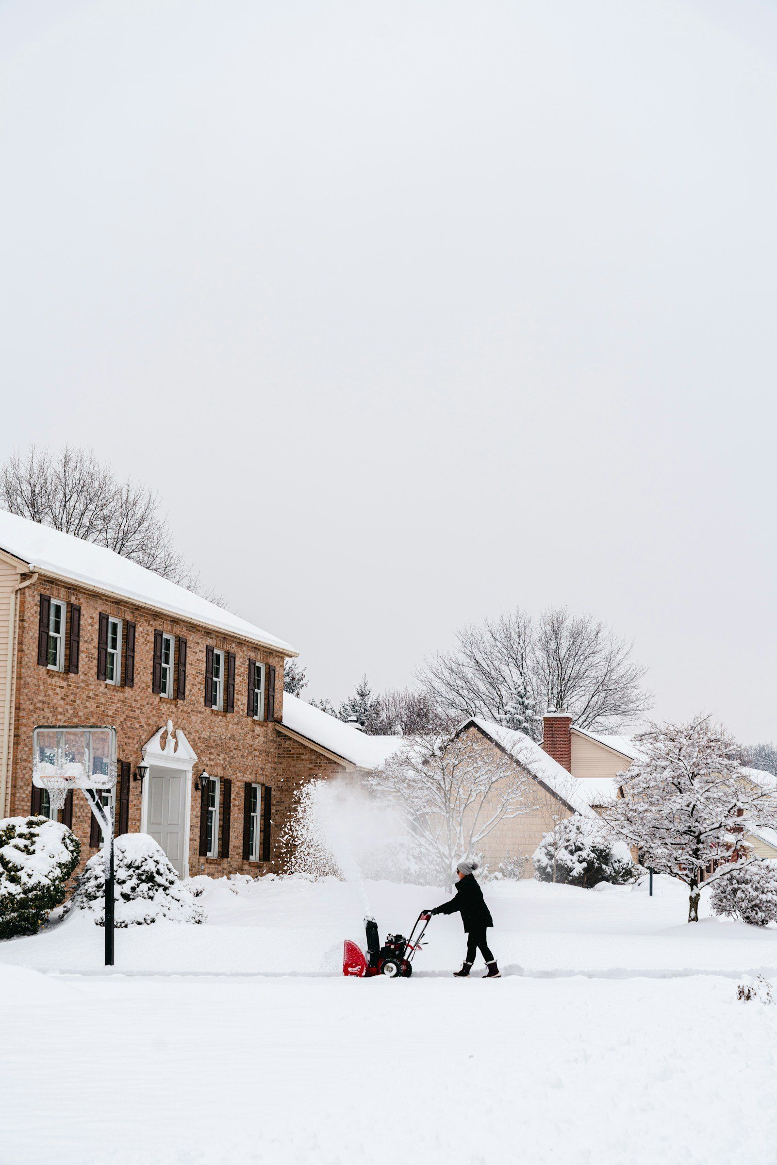 Clearing a snowy driveway with a snow blower in front of a brick home