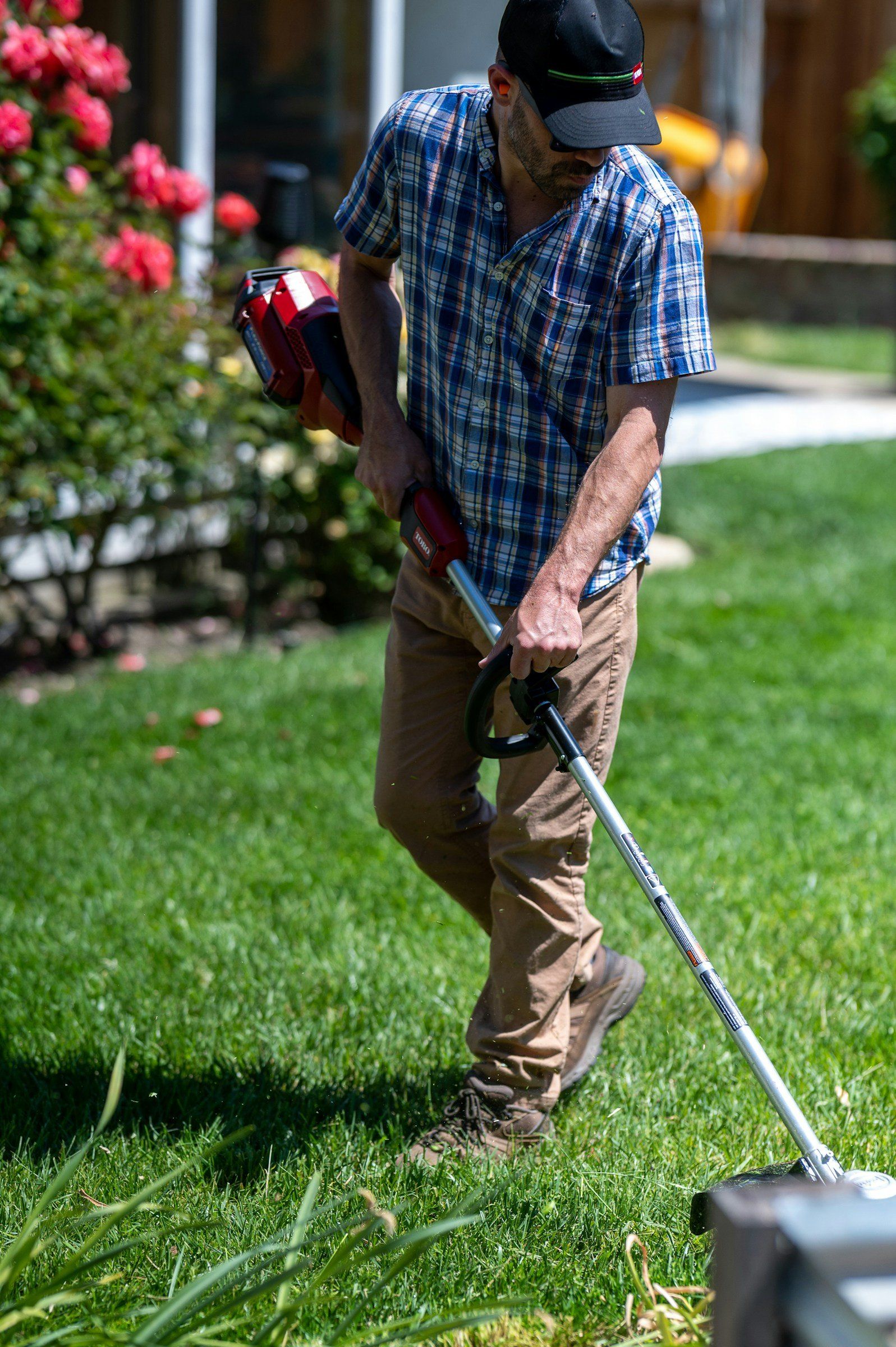 Crew member edging a sunny lawn with a string trimmer